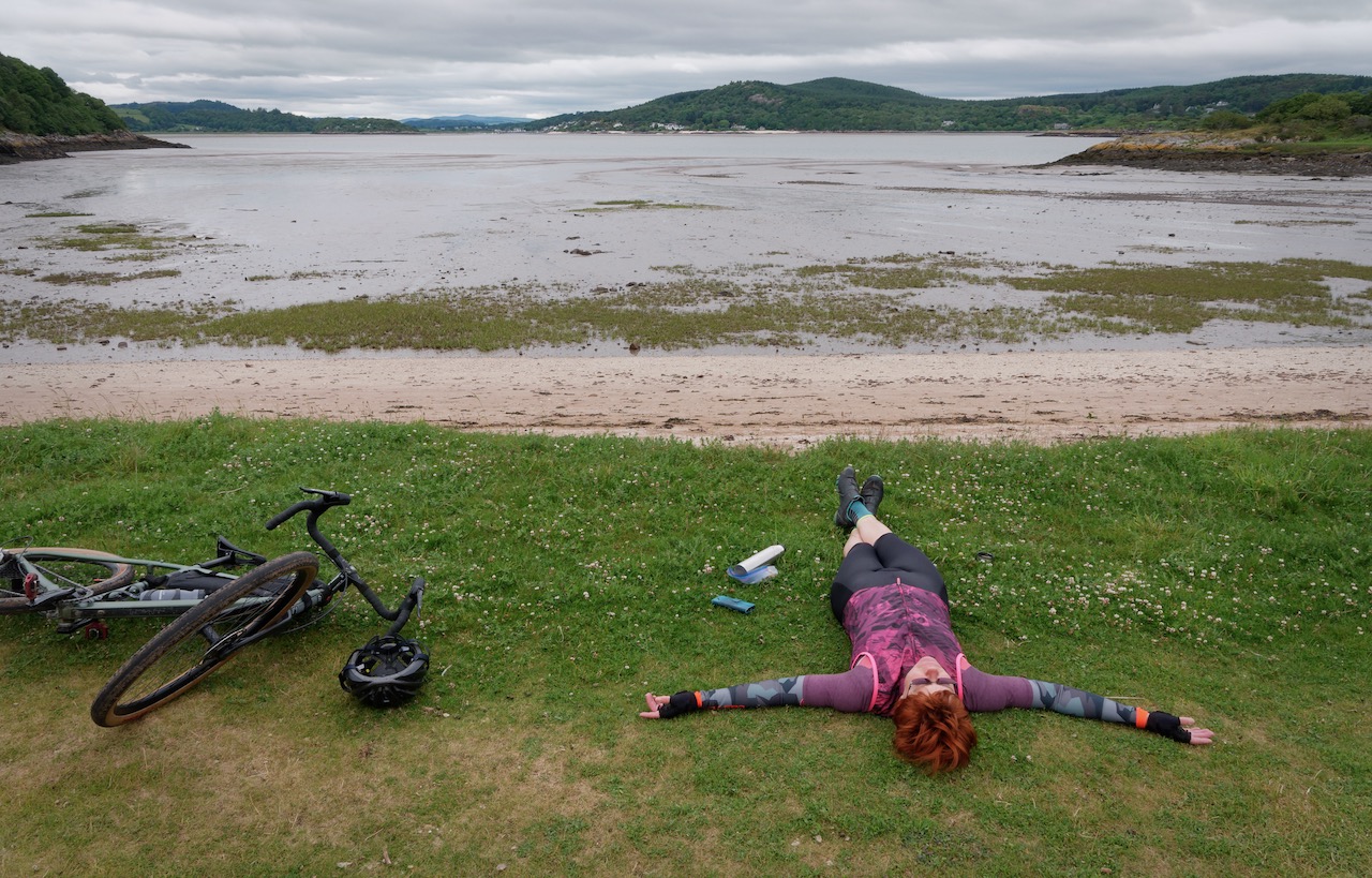 Cyclist lying on grass beside sea